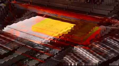 Hot metal piece glowing orange-red in a factory, with a surrounding industrial background.