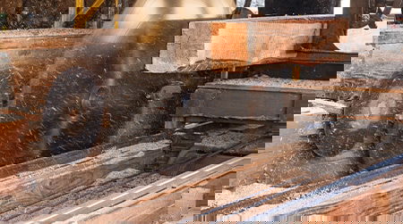 Wooden plank passing through a saw, with sawdust scattering around.