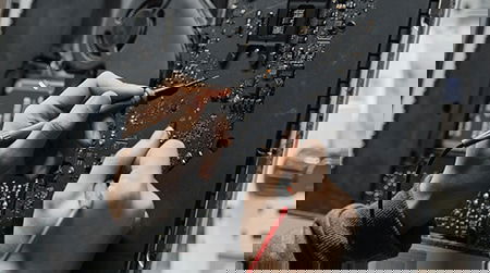 Close-up of a person soldering wires onto a motherboard with other electronic components visible.
