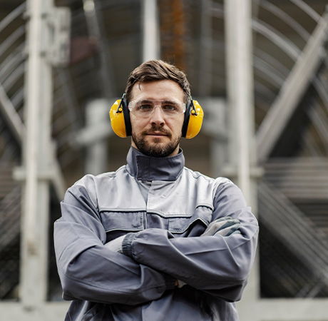 A man wearing safety earmuffs and workers clothes looking at the camera.